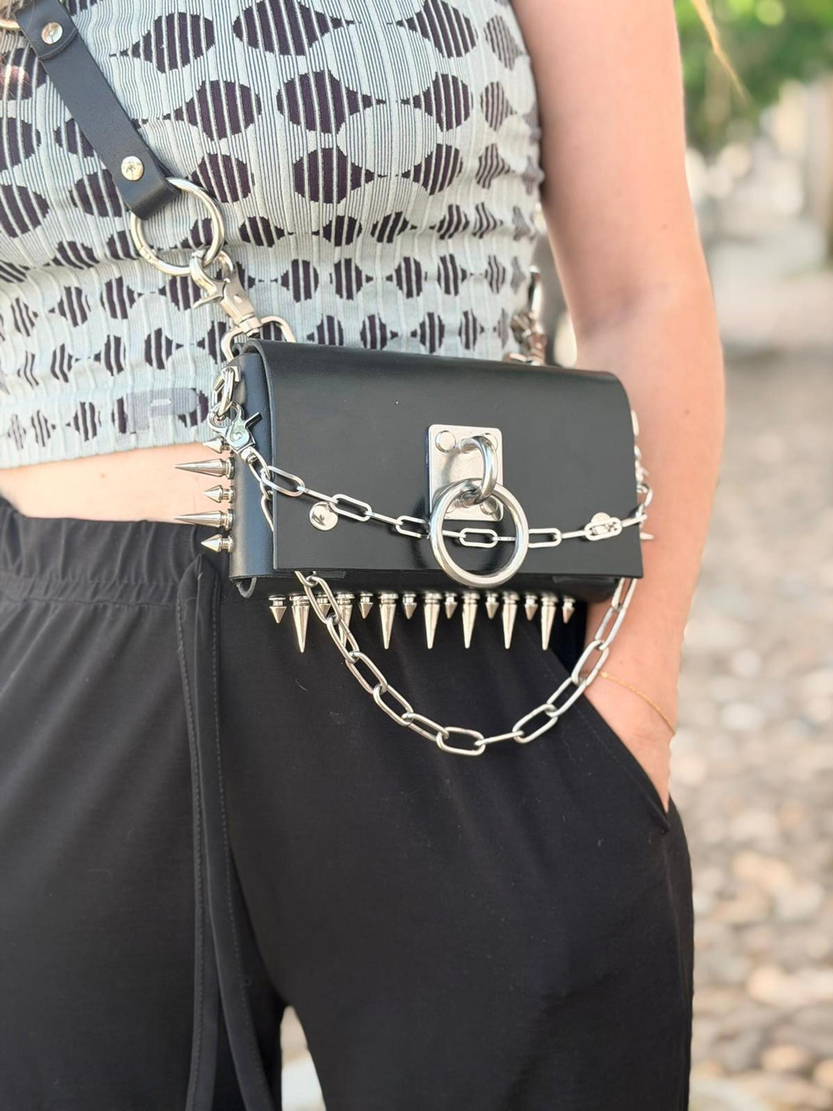 Side view of model, black spiked leather bag as hip bag, studded strap and chain accent