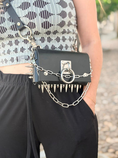 Side view of model, black spiked leather bag as hip bag, studded strap and chain accent