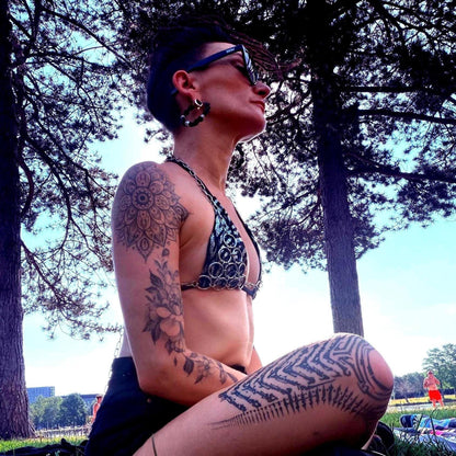 Side profile of seated model in sunlight wearing chainmail bra top and shorts, rave outfit energy visible