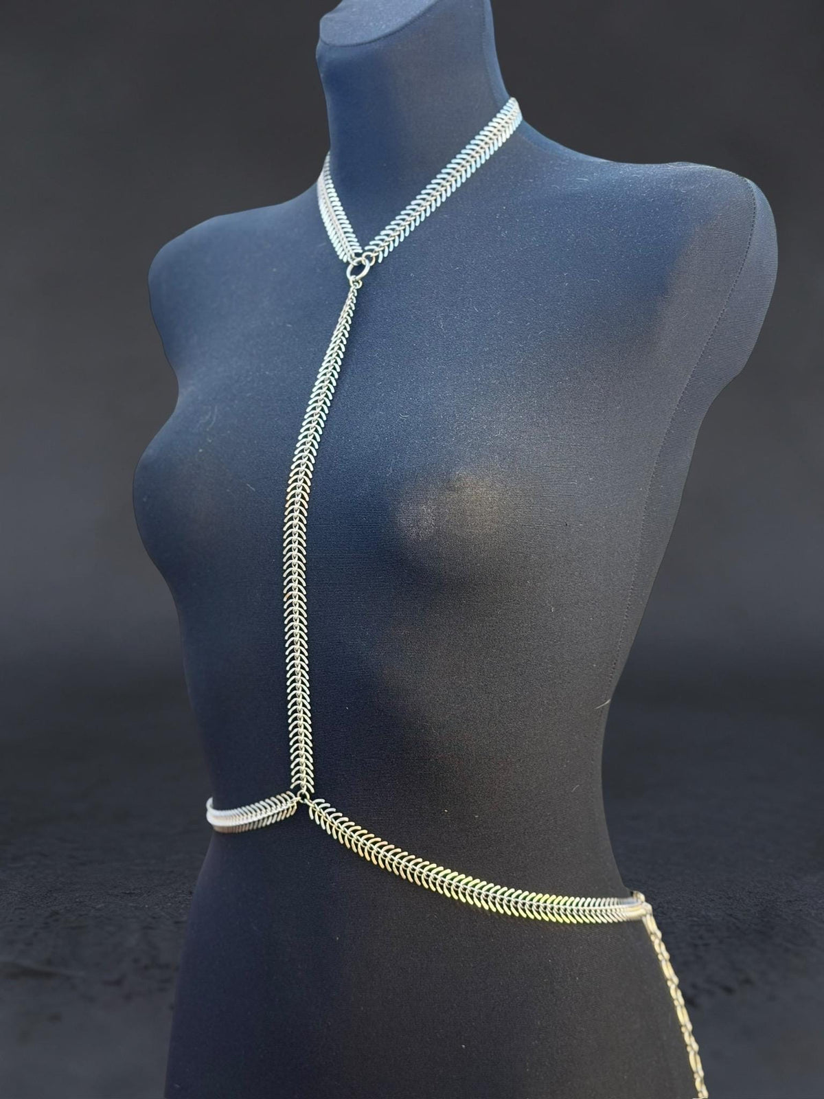 Angled blue mannequin displays spine body chain, minimalist stainless steel harness, Y-shaped neck and waist chain