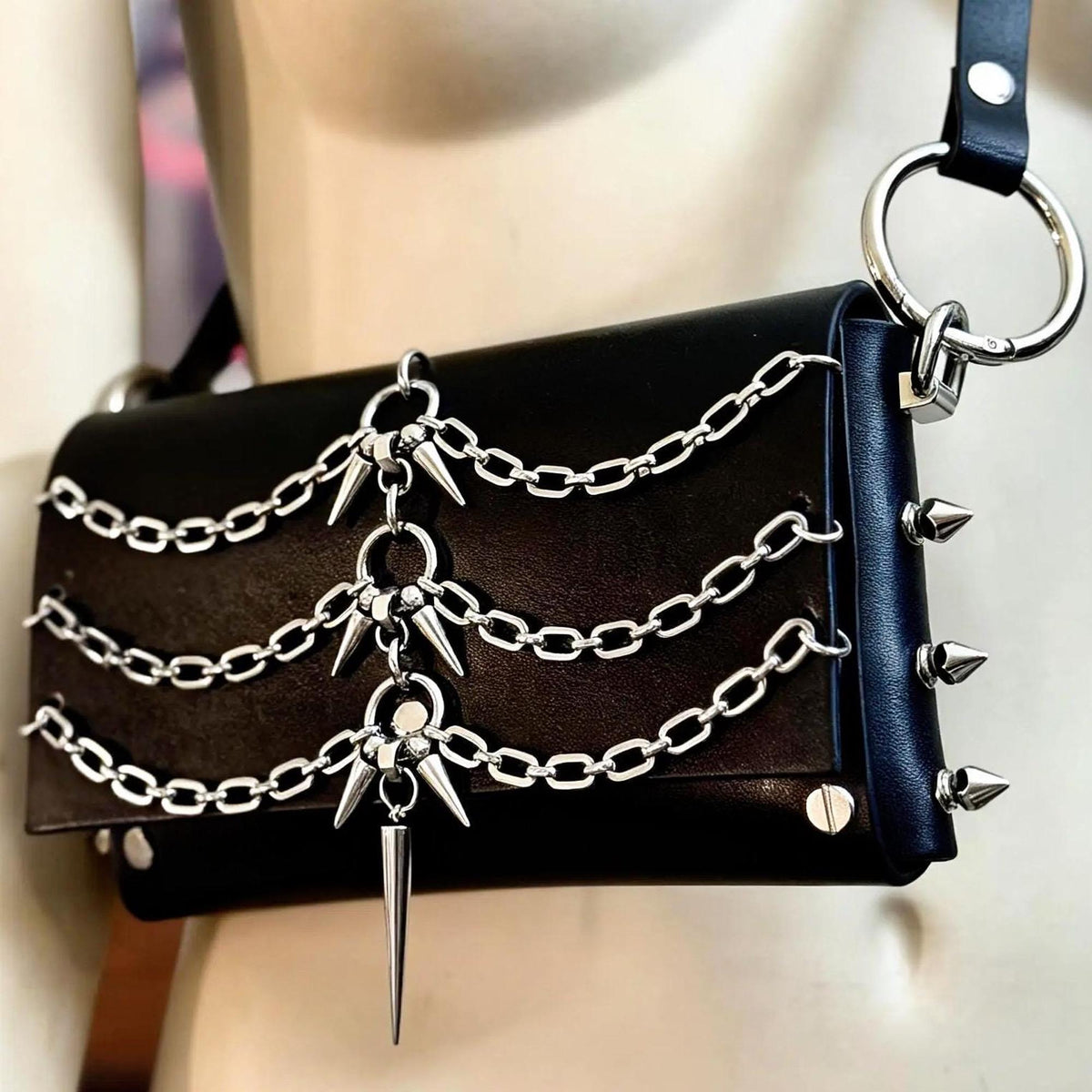 Angled close up of O ring and riveted side spike studs, modular belt style punk crossbody bag