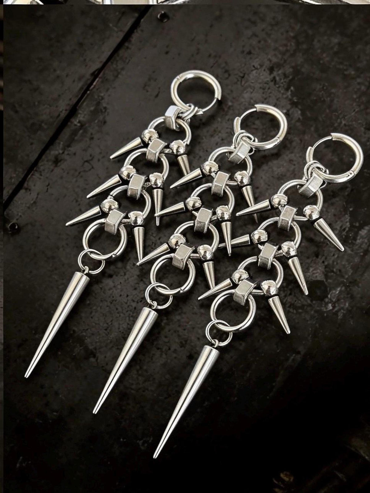 Three pairs fanned on dark backdrop, chainmail spike earrings highlighting silver-tone finish and elongated silhouette
