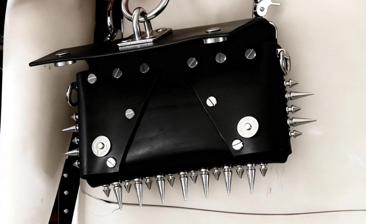 Flat-lay like close-up, black spiked leather bag lower edge dense spikes, stainless studs and rivets
