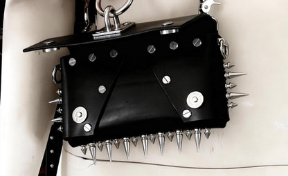 Flat-lay like close-up, black spiked leather bag lower edge dense spikes, stainless studs and rivets