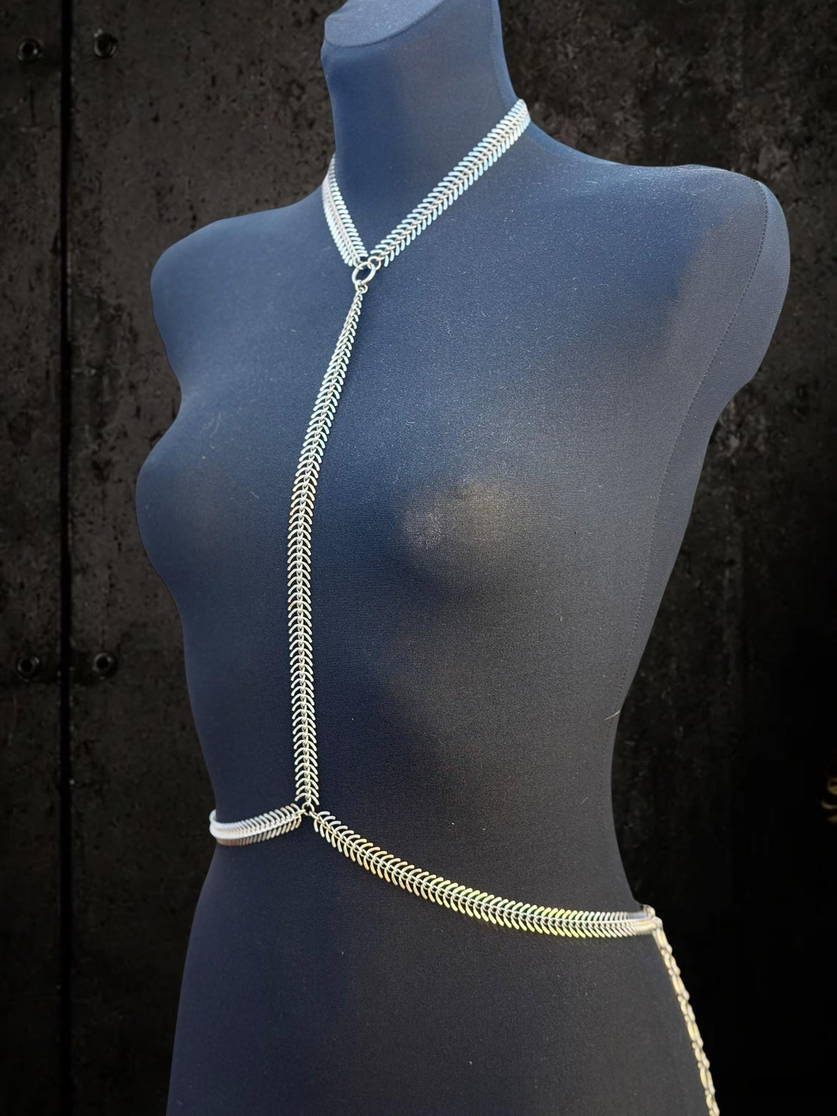 Tilted blue mannequin wearing spine body chain, sleek vertebrae body chain design in durable stainless steel finish