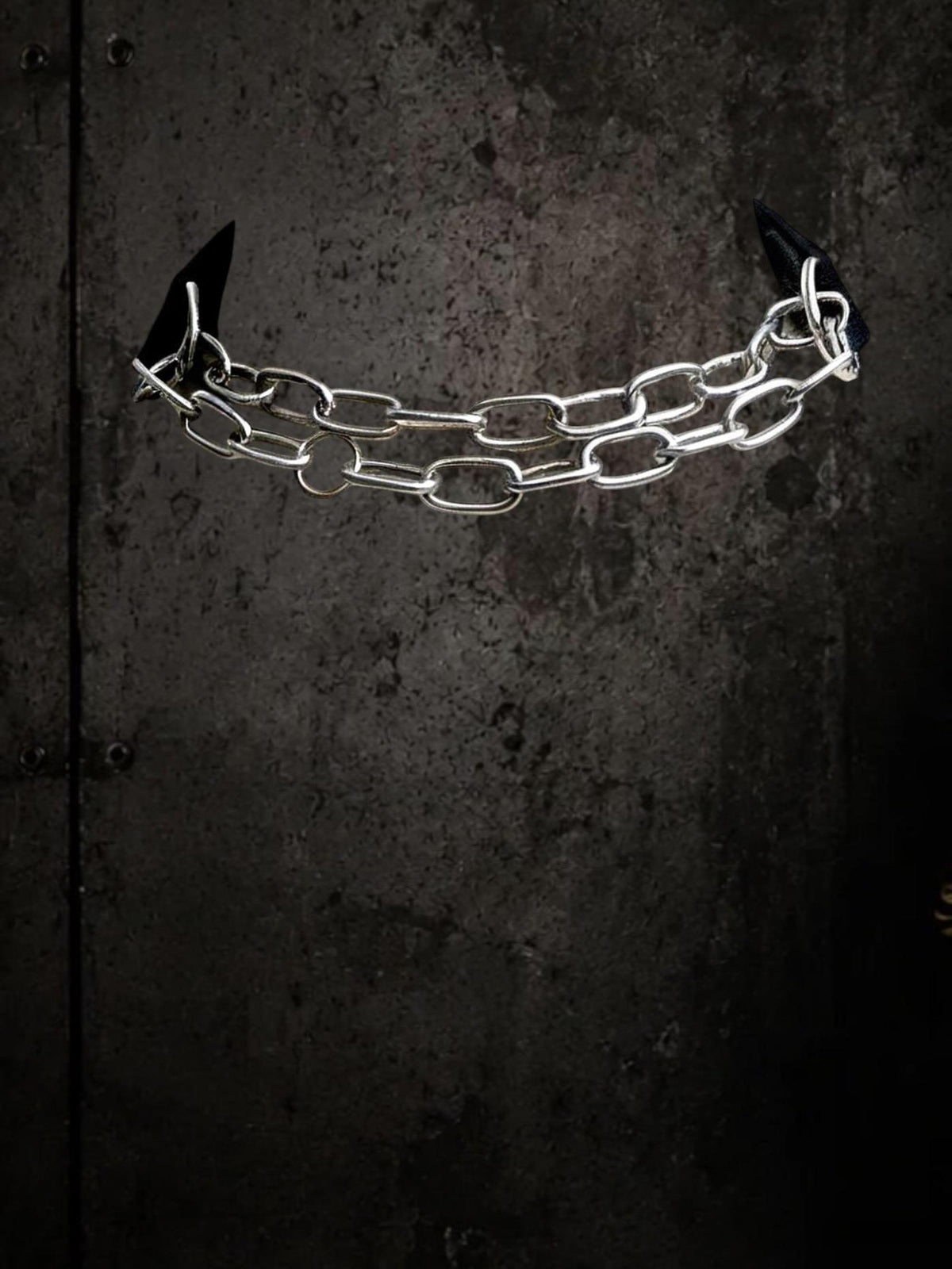 Single removable chain component suspended against dark wall, stainless steel links for modular choker.