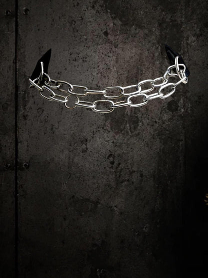 Single removable chain component suspended against dark wall, stainless steel links for modular choker.